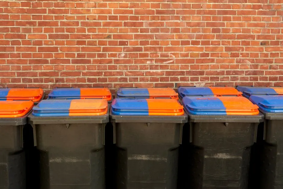 Row of recycling bins with vibrant lids in front of a brick wall for urban waste management.