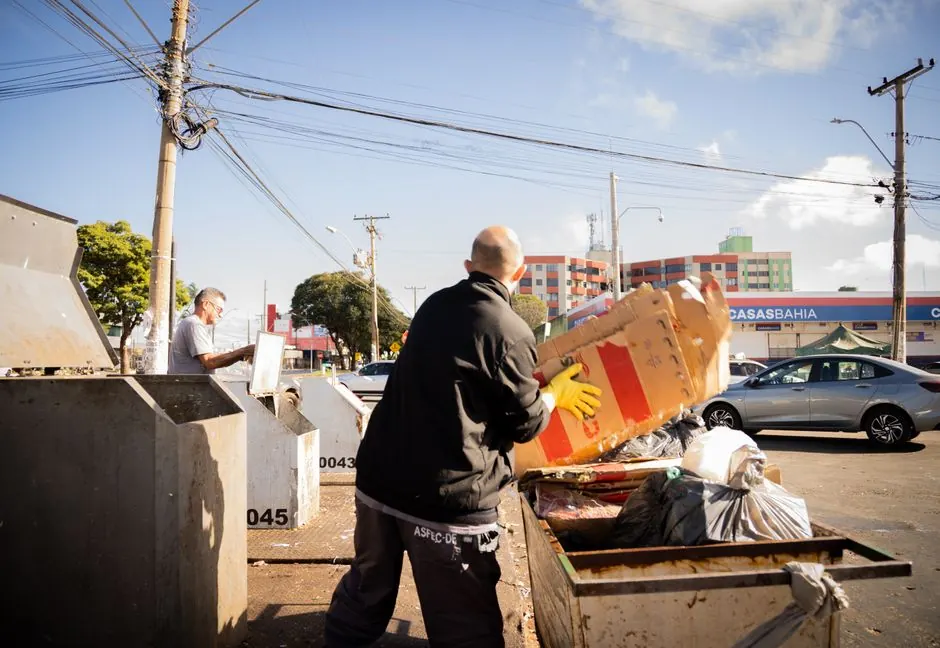Two workers handling waste disposal in an urban environment on a sunny day.